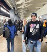 A man wearing a social media themed shirt while the holiday subway rests on the left at 2nd Ave Station